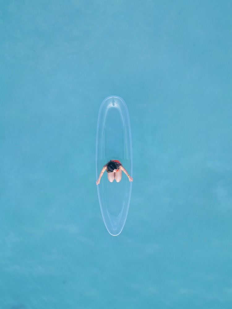 A creator on a transparent paddle board in bright blue water